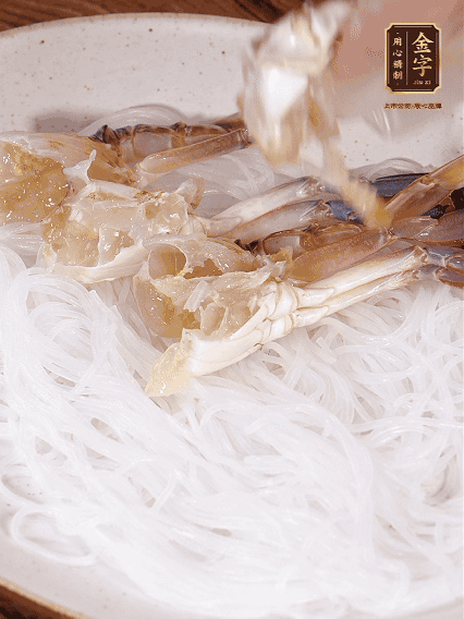 盤底墊上粉絲，擺上梭子蟹、火腿片，撒姜粒，淋上蒸魚豉油、花雕酒調(diào)味腌制15分鐘